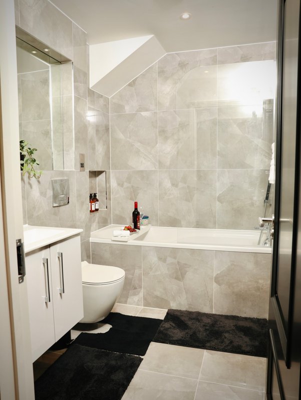 Modern bathroom with white vanity, toilet, bathtub with glass enclosure and marble-look tiling