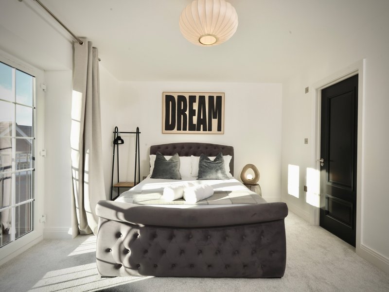 Bright modern bedroom with double bed, dark headboard, wall art saying DREAM, and ottoman seating