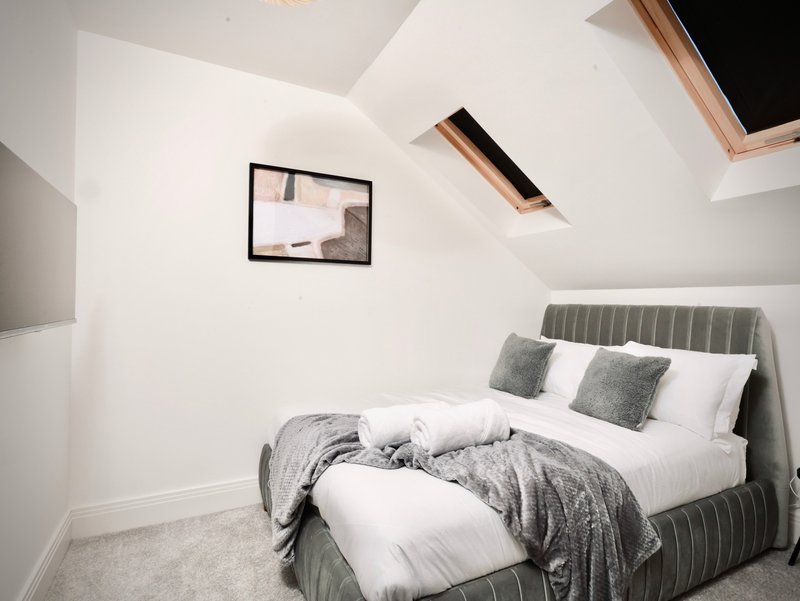 Modern bedroom with grey upholstered bed, white bedding, skylights and framed wall art