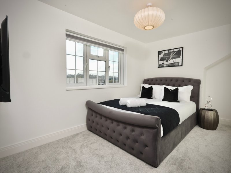 Modern bedroom with grey upholstered bed, white and black bedding, large window and ceiling light