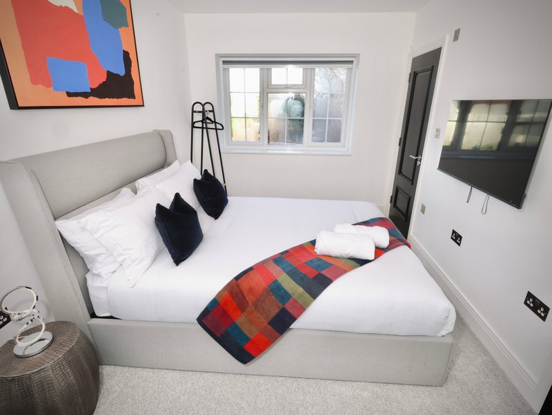 Modern bedroom with grey upholstered bed, white bedding, colourful throw and black cushions