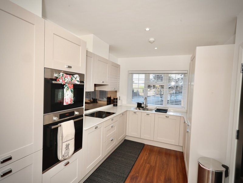 Modern white kitchen with integrated appliances, wooden flooring and window overlooking garden