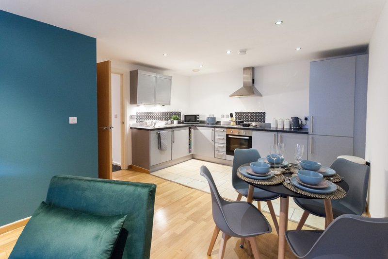 Open-plan kitchen and dining area with teal accent wall, wooden flooring, and dining table set