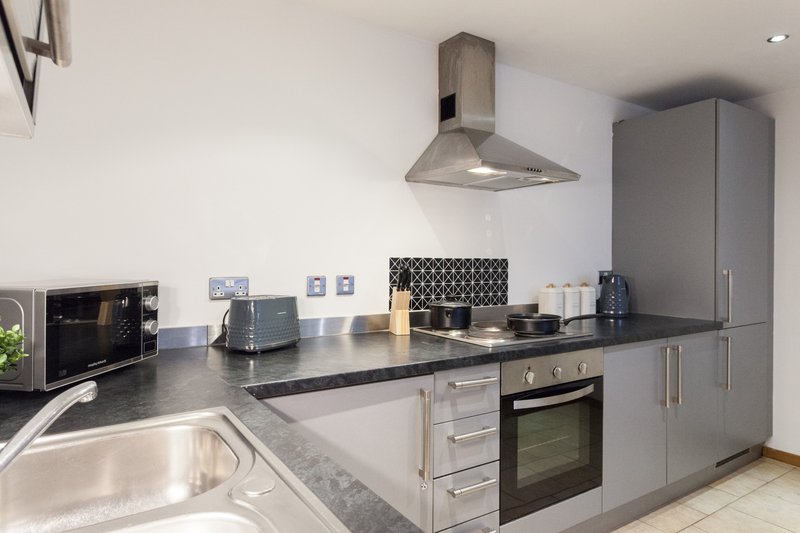 Modern kitchen with grey cabinetry, black countertop, stainless steel appliances and range hood