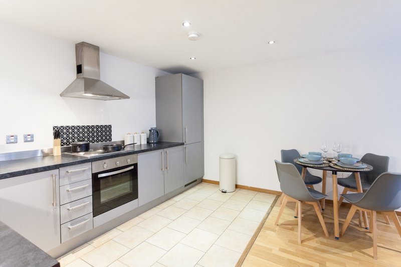 Modern kitchen with grey cabinetry, stainless steel appliances, and adjoining dining area with wooden table and grey chairs
