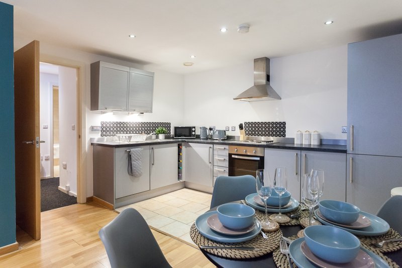 Modern kitchen and dining area with blue cabinetry, dining table set for four, and wood flooring