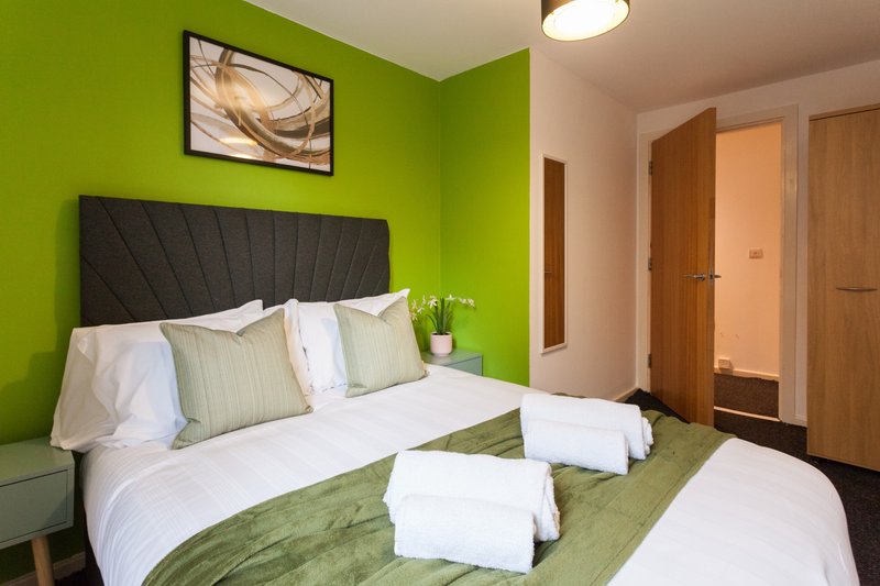 Bright bedroom with lime-green walls, black padded headboard, double bed with white linens and green cushions