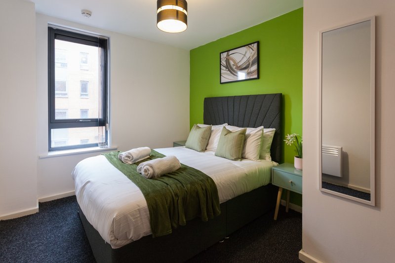 Modern bedroom with double bed, green accent wall, window and en-suite door