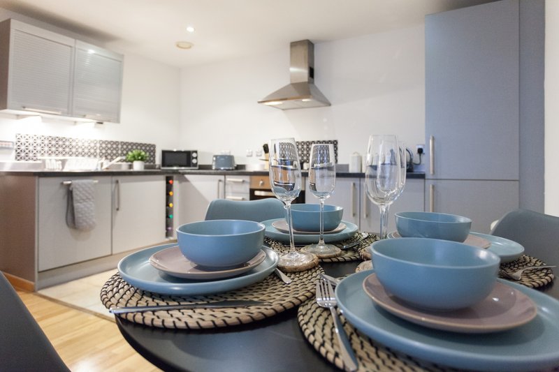 Modern kitchen with dining table set with blue dishware, glasses and woven placemats