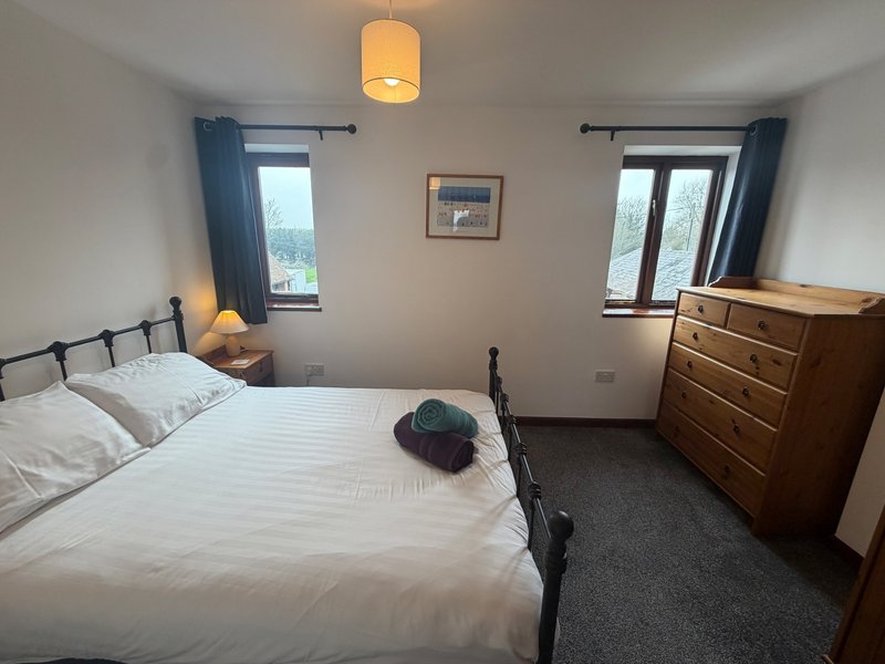 Bedroom with double bed, wooden dresser, two windows with blue curtains and pendant light