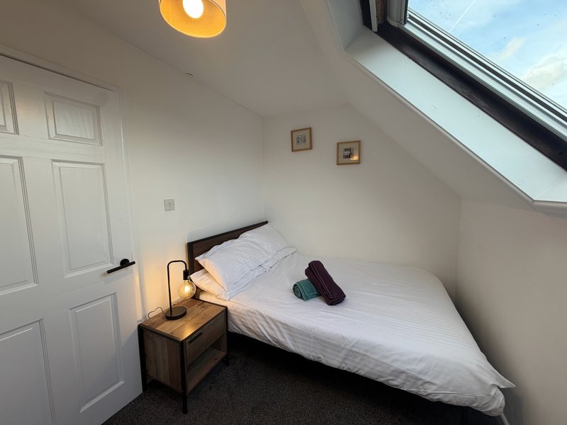 Bright attic bedroom with single bed, wooden nightstand, pendant light and skylight