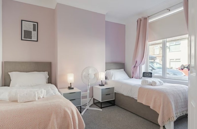 Twin bedroom with two beds, bedside table, lamp, fan, and pink-painted walls