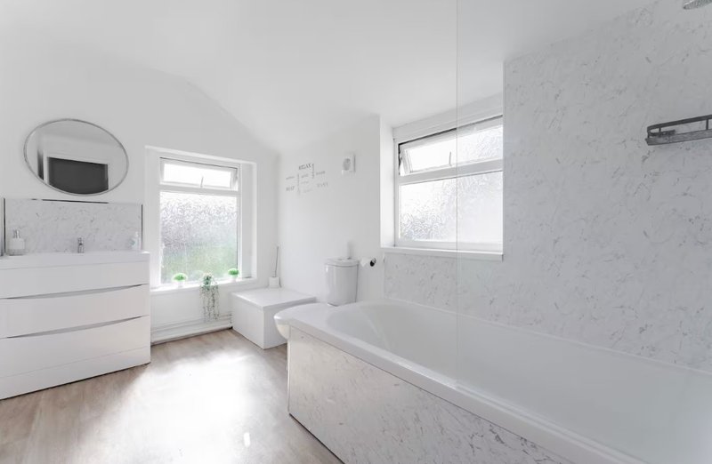 Modern bathroom with white marble tiles, freestanding bathtub, vanity sink and mirror