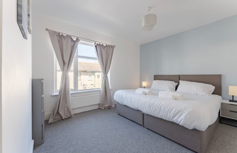 Modern bedroom with double bed, grey headboard, window with curtains and blue feature wall
