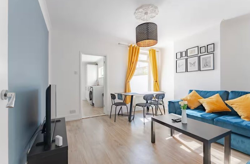 Modern living room with blue sofa, dining table, yellow curtains and wooden flooring