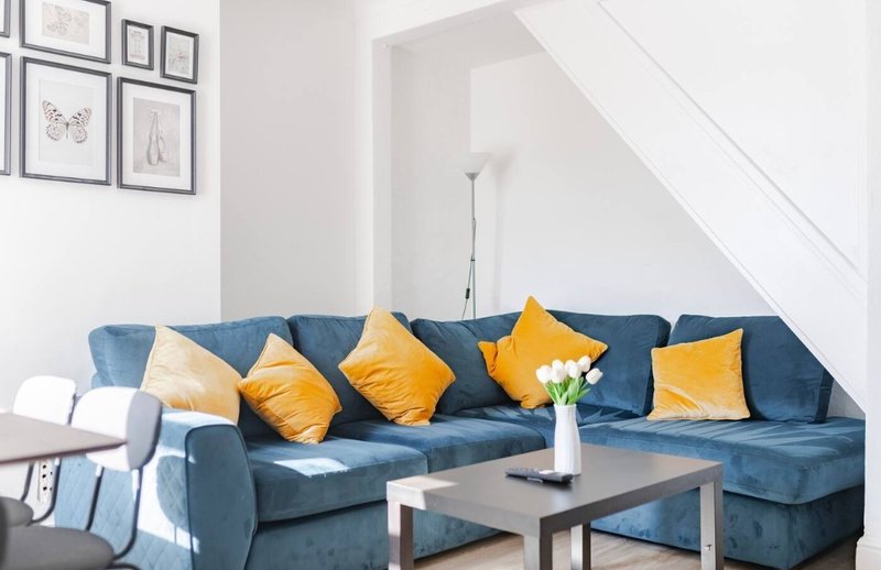 Modern living room with blue corner sofa, yellow cushions, dark coffee table and wall art