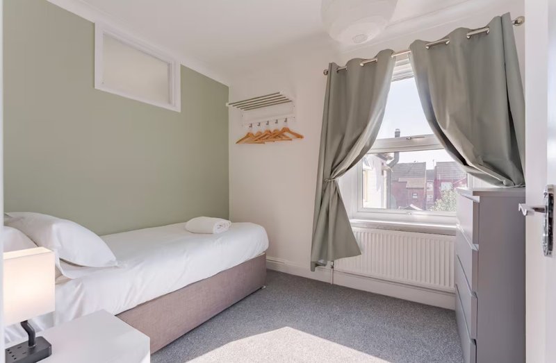 Bright bedroom with single bed, green accent wall, large window with curtains and city view