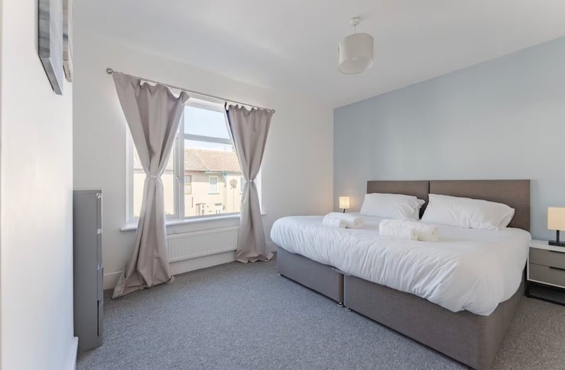 Bright bedroom with double bed, large window with curtains, and light blue accent wall