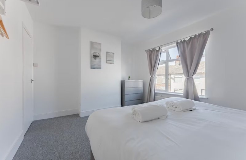 Bright bedroom with double bed, grey carpet, white walls, window with curtains