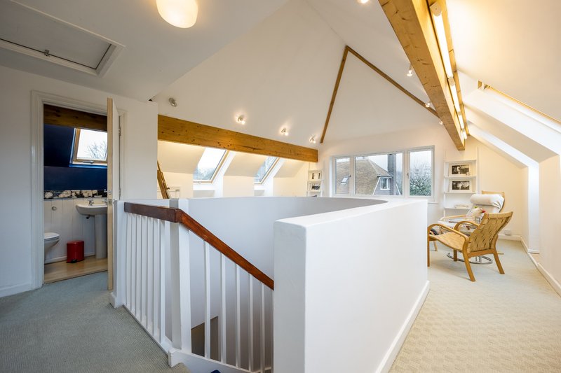 Bright attic bedroom with skylights, white partition wall, wooden beams and rattan chair