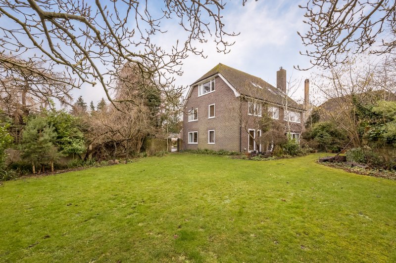 Brick country house with manicured lawn, bare trees and mature garden surroundings
