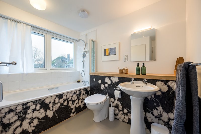 Modern bathroom with white suite, pedestal sink, bathtub, black and white tile walls, mirror and window.