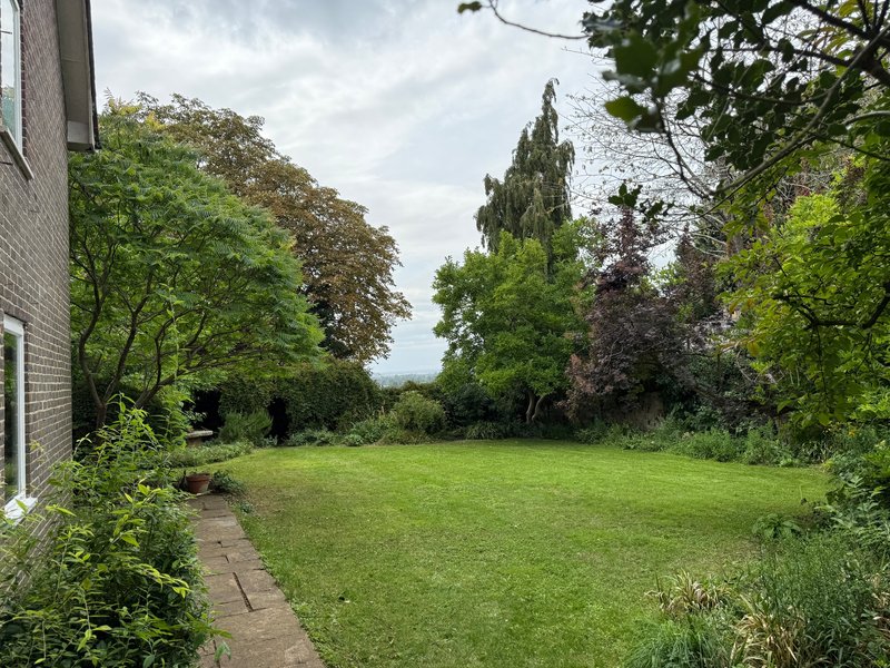 Large garden with manicured lawn, mature trees, and brick house exterior visible