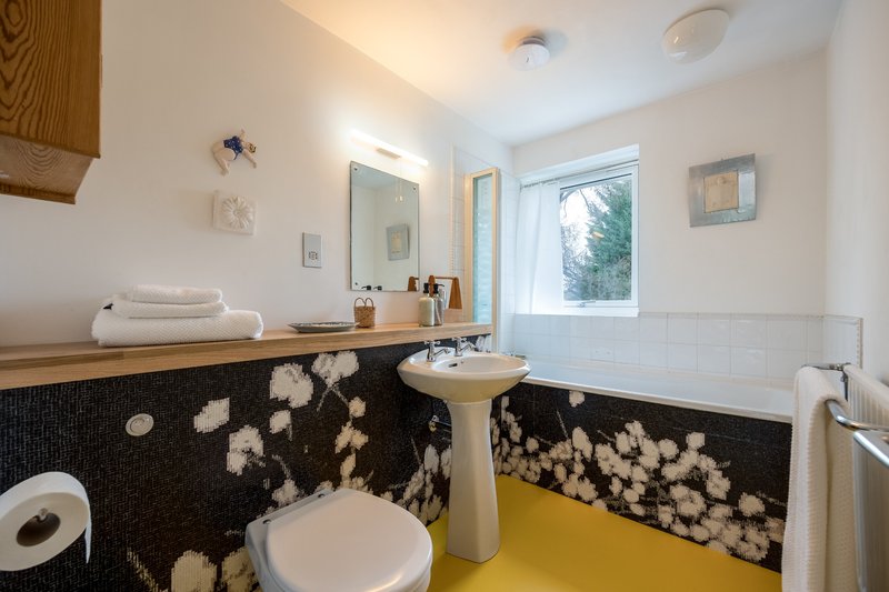 Modern bathroom with pedestal sink, toilet, bathtub, black and white tile, yellow floor