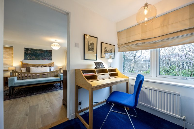 Bedroom with wooden desk, blue chair, and view through open door to bed area