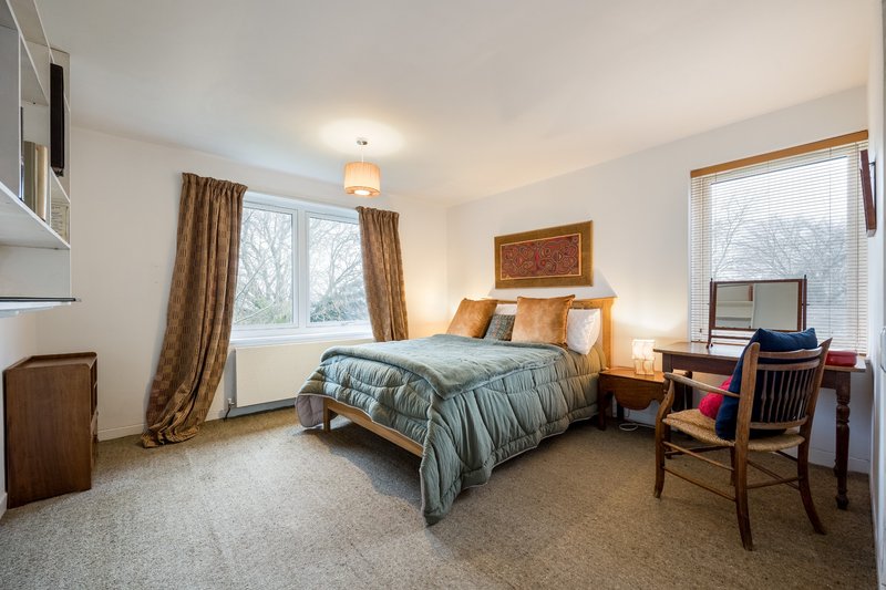 Spacious bedroom with double bed, wooden furniture, desk area and large windows with curtains