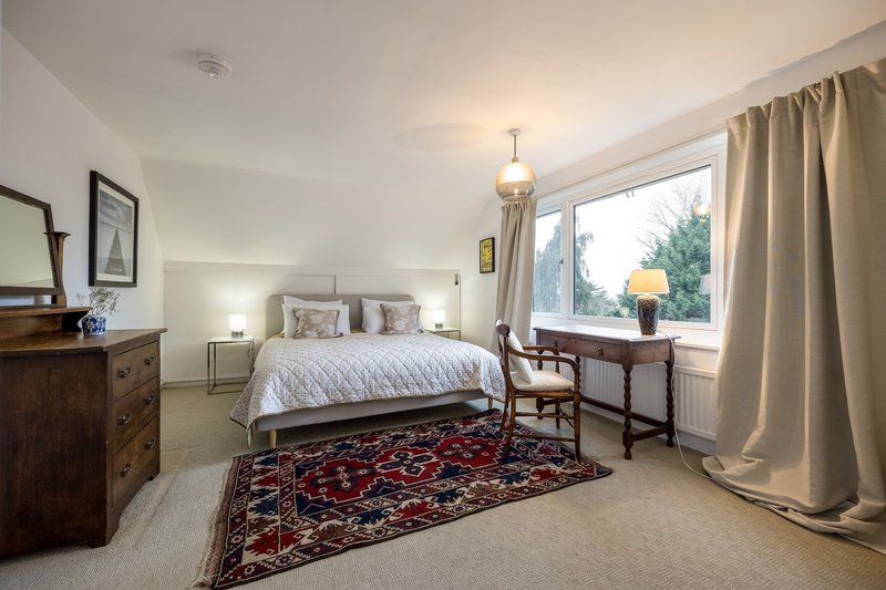 Spacious bedroom with double bed, wooden furniture, patterned rug and large window