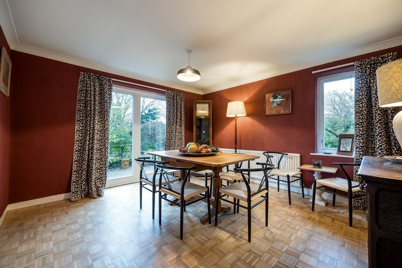Dining room with burgundy walls, wooden table, modern chairs and garden views