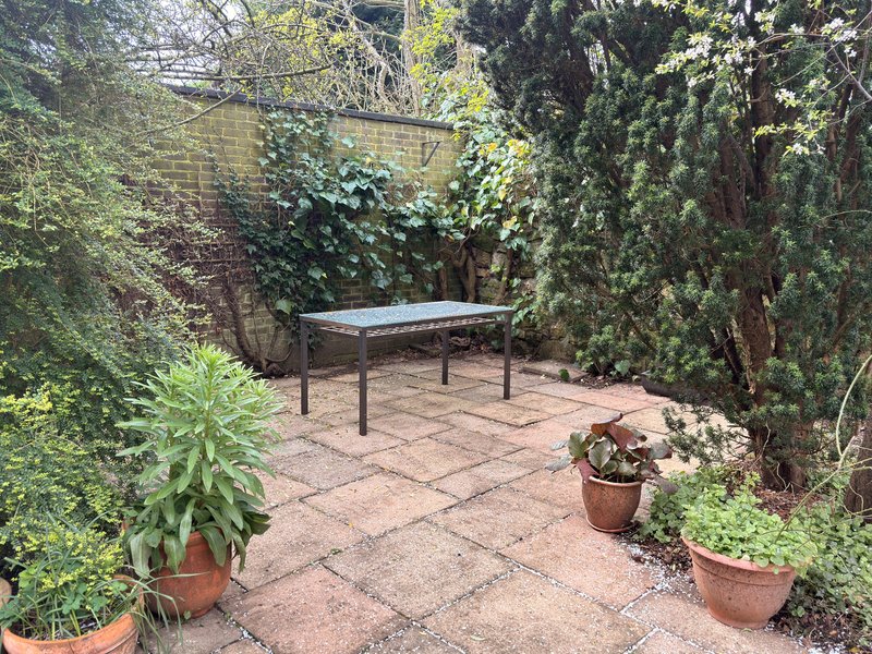 Garden patio with table, potted plants, and ivy-covered brick walls