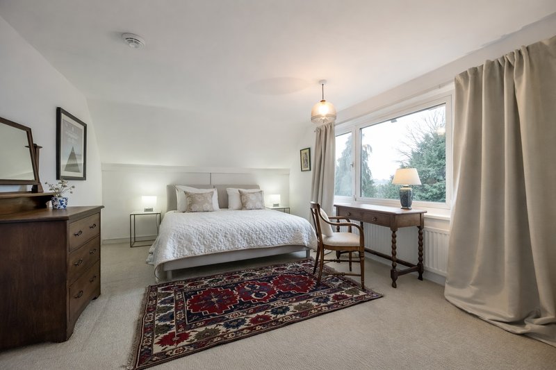 Bright bedroom with double bed, wooden furniture, patterned rug and large windows