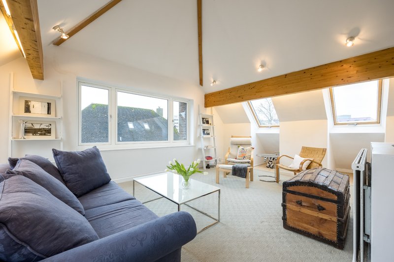 Modern open-plan living space with blue sofa, glass coffee table, wooden beams and skylights