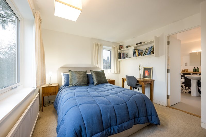 Bright bedroom with blue duvet, wooden furniture, shelving, and large window with natural light
