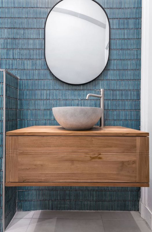Modern bathroom with oval mirror, wooden vanity and stone vessel sink