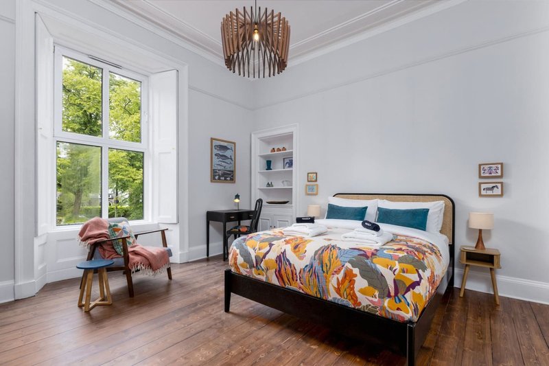 Bright bedroom with double bed, wooden floor, large window and wooden ceiling lamp