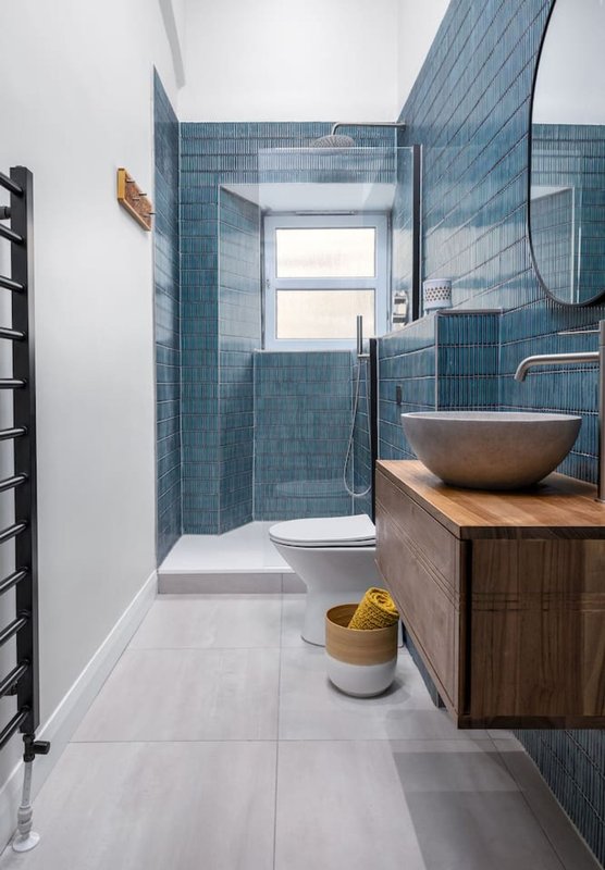 Modern bathroom with blue tile walls, wooden vanity, vessel sink, and walk-in shower