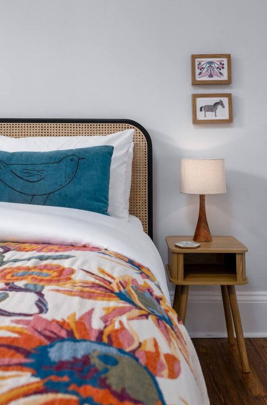 Bedroom with rattan bed frame, colorful bedding, wooden nightstand with lamp and framed wall art
