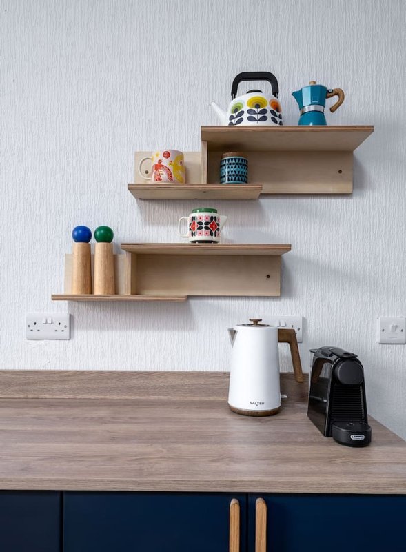 Kitchen countertop with wooden shelves displaying kettles, mugs, decorative items and small appliances