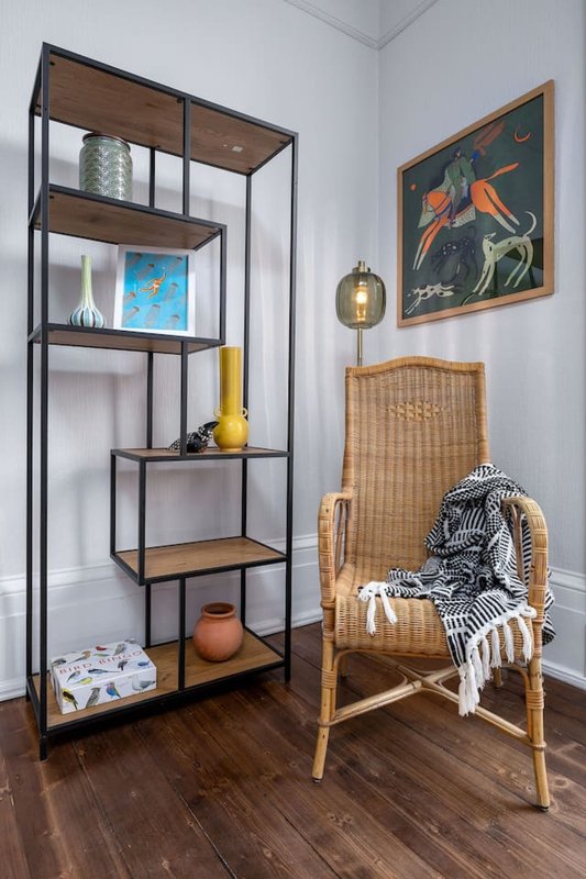 Corner of room with metal shelving unit, wicker chair, framed artwork, and wooden flooring