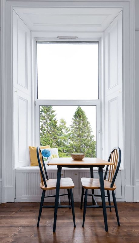 Dining nook with two wooden chairs, small table, window seat with cushions and garden view