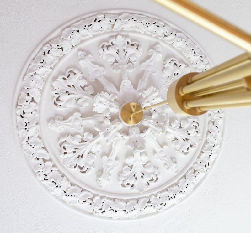 Ornate white ceiling rose with brass pendant light fixture mounted centrally