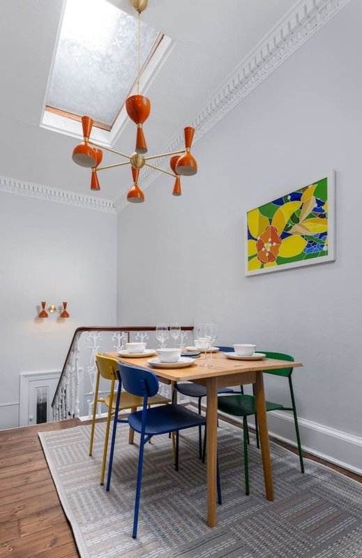 Dining room with wooden table, blue chairs, orange pendant light fixture and colorful wall art