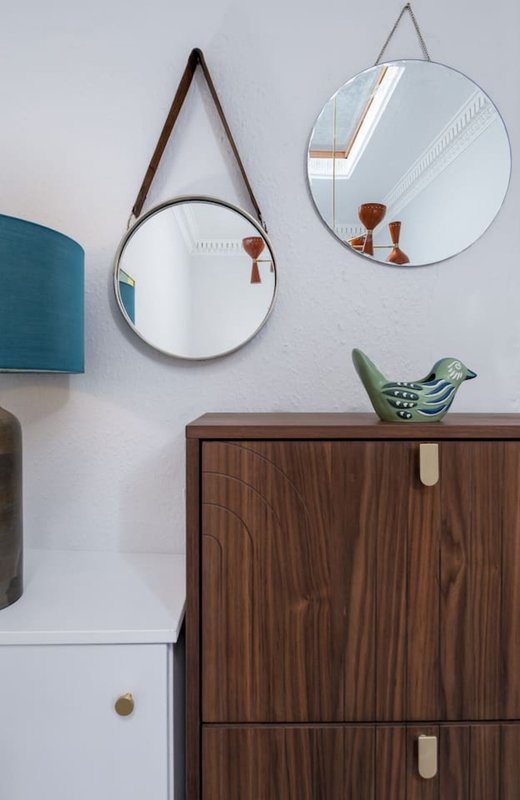 Modern bathroom wall with two round mirrors, wooden cabinet, and green ceramic bird decoration