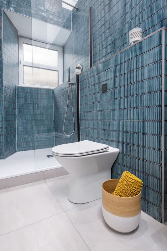 Modern bathroom with blue tile walls, white toilet, walk-in shower and woven storage basket