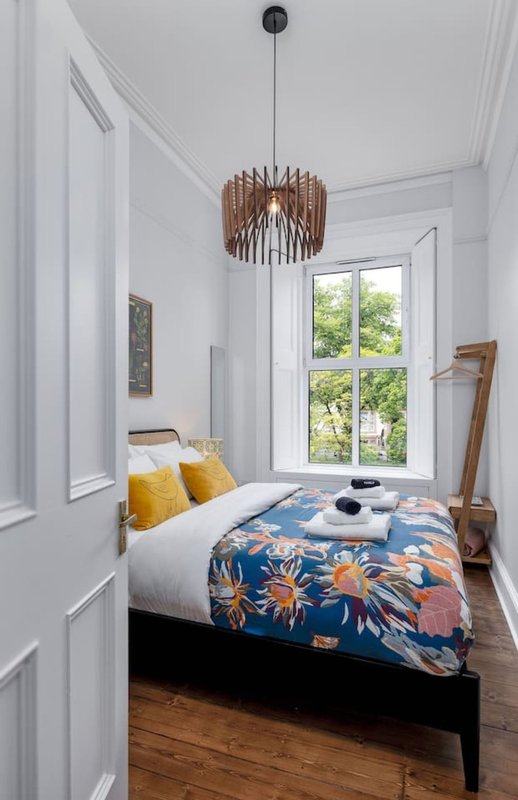 Bright bedroom with single bed, wooden pendant light, yellow cushions and patterned duvet