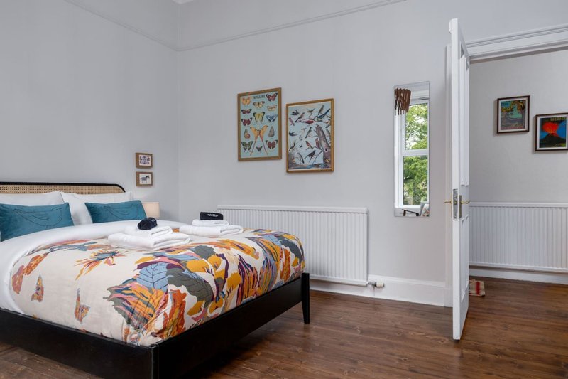 Bright bedroom with double bed, colorful bedding, framed artwork, wooden flooring and glass doors