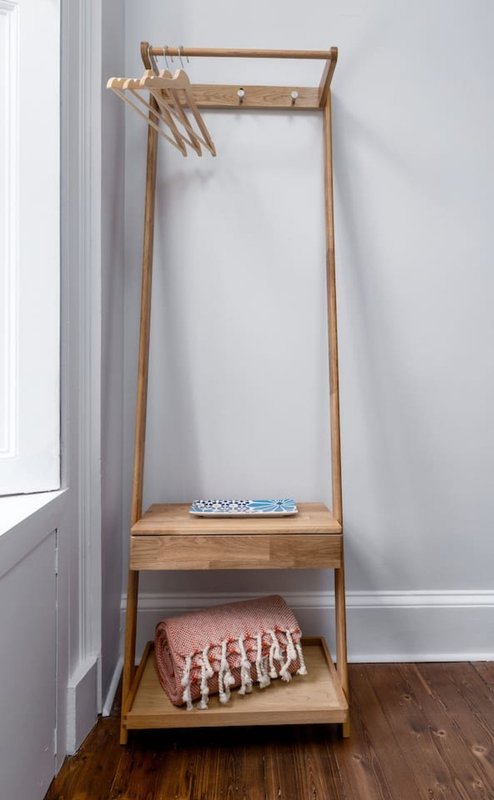 Wooden clothing rack with hangers, shelf and storage, against white wall